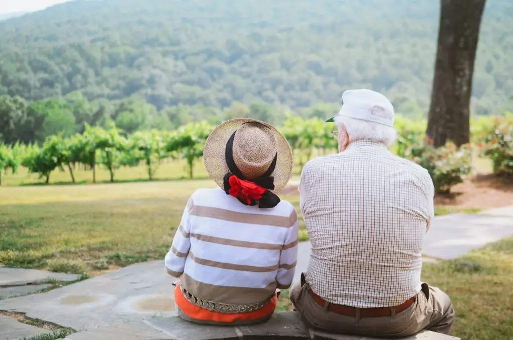 elderly couple sitting on pathway overlooking a forest view